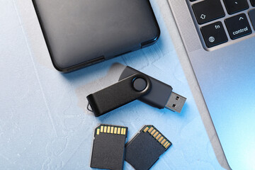 Flash drive, SD memory cards, external hard disk and laptop on light grey table, flat lay