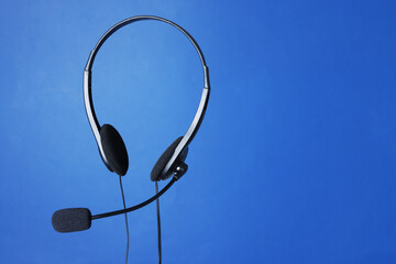 Headset with microphone in air on blue background, space for text