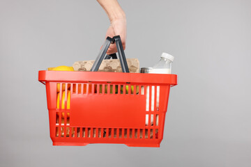 Fototapeta premium Man holding shopping basket with different products on grey background, closeup