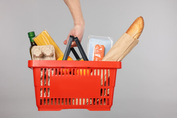 Man holding shopping basket with different products on grey background, closeup