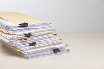 File folders with papers and binder clips on wooden table against light background, space for text