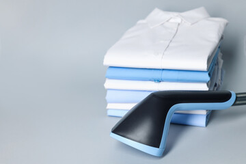 Upright steamer and stack of folded shirts on grey background, closeup. Space for text
