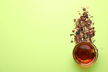 Delicious herbal tea in glass cup and dry leaves on light green background, flat lay. Space for text