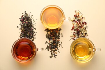 Different freshly brewed teas and dry leaves on beige background, flat lay