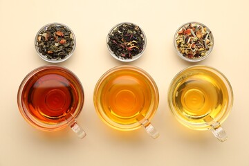 Different freshly brewed teas and dry leaves on beige background, flat lay
