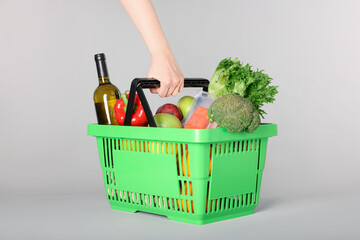 Woman with shopping basket full of products on gray background, closeup