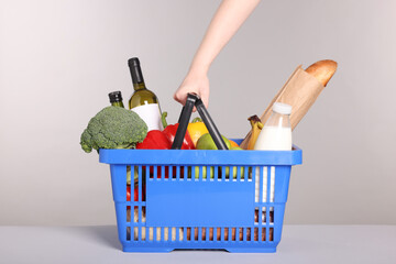 Woman with shopping basket full of products on gray background, closeup