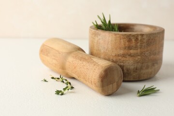 Wooden mortar with rosemary, thyme and pestle on white table, closeup