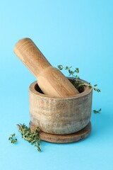 Wooden mortar with thyme and pestle on light blue background, closeup