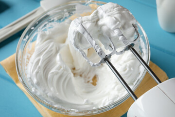 Hand mixer with whisks and whipped cream on light blue table, closeup