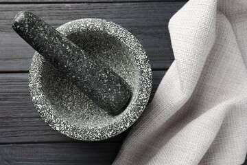 Stone mortar and pestle on black wooden table, top view
