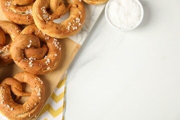 Tasty pretzels with salt on white marble table, flat lay. Space for text