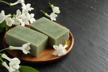 Bars of soap and jasmine flowers on black table, closeup. Space for text