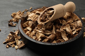 Pieces of dry chicory roots in bowl and scoop on dark textured table, closeup