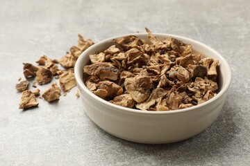 Pieces of dry chicory roots in bowl on gray textured table, closeup