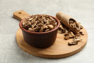 Pieces of dry chicory roots in bowl and scoop on gray textured table, closeup