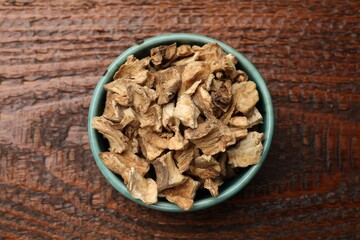 Pieces of dry chicory roots in bowl on wooden table, top view