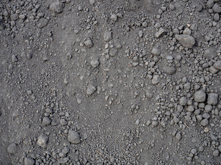 Close-up of dark soil texture with pebbles, representing fertile land.