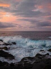 Beautiful sunset on the beach of the Atlantic Ocean: pink soft light, blue waves, rocky black shore and clouds on the horizon. Mesa del Mar, Tenerife, Canary Islands, Spain.