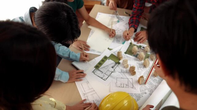 Architect and safety engineer discussion about building construction use blueprint on table with architectural document, measurement tool and wooden block scatter around at modern office. Delineation.