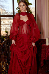 young and beautiful girl in long red evening red dress posing in interior