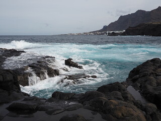 Volcanic coast of Tenerife island: blue water of Atlantic ocean, black rocky shore and lava rocks on the horizon. Holidays in Canary Islands, Spain.