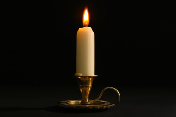 Burning candle in candlestick on black background