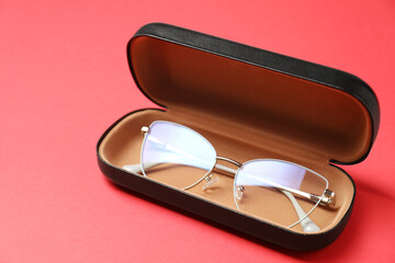 Case with stylish glasses on red background, closeup