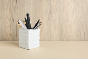 Ballpoint pens in holder on beige table against wooden background. Space for text