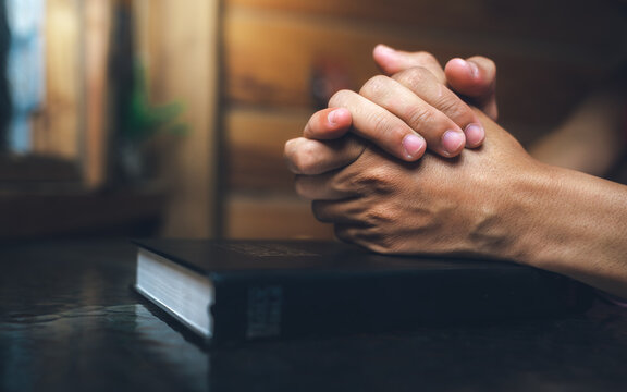 Close up of a man praying, hands clasped together on Bible, devotional concept.
