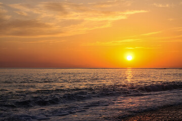 beautiful and colorful sunset, warm light and many clouds, sea waves on the sea coast