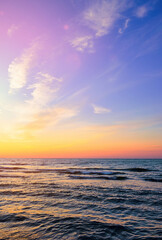 Obraz premium Colorful sunset over a calm sea with gentle waves and a vibrant sky. Serene ocean landscape perfect for travel, relaxation, or nature theme