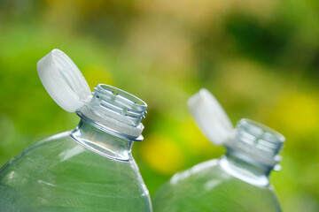 Plastic bottles with so-called tethered caps against a green blurry background. The caps are attached to the drink bottle to prevent it from ending up in nature. The EU bans loose closures and caps.