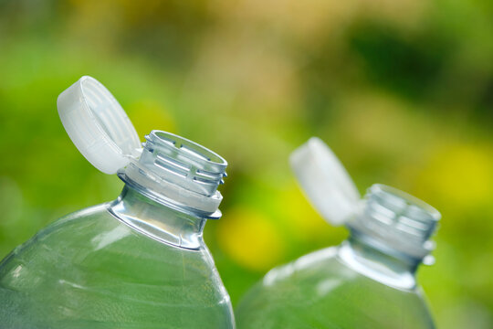 Plastic bottles with so-called tethered caps against a green blurry background. The caps are attached to the drink bottle to prevent it from ending up in nature. The EU bans loose closures and caps.