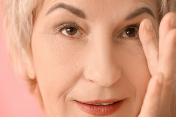 Mature woman putting in contact lenses on pink background, closeup