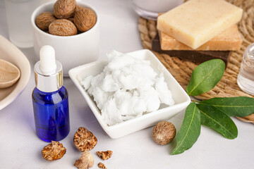 Bowl with shea butter, nuts and cosmetic products on light table