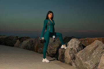 person in workout attire performs pose dumbbells against rocky backdrop during twilight. captures blend of fitness and natural beauty in evening light.