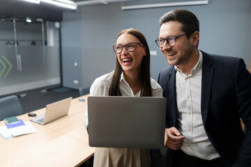 Excited business colleagues laughing happily as working together with laptop in the office in board meeting room