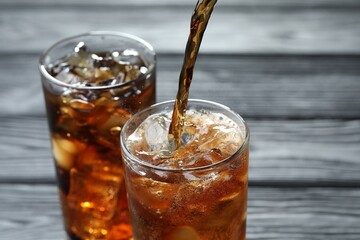 Pouring refreshing cola into glass at grey wooden table, closeup