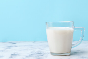 Cup of milk on white marble table against light blue background. Space for text