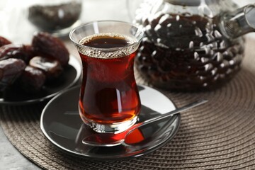 Traditional Turkish tea in glass cup, teapot and dates on table, closeup