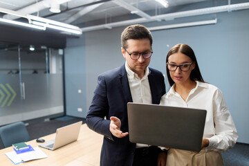 Two professional business people working in office with laptop computer, executive manager talking to female colleague, having conversation