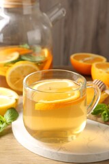 Aromatic fruit tea in glass cup, teapot, orange, lemon, honey and mint on wooden table, closeup