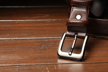 One brown leather belt on wooden table, closeup. Space for text