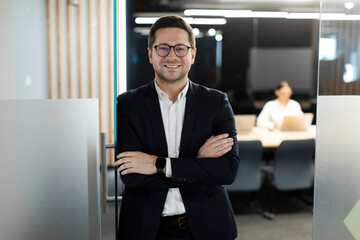 Portrait of successful European businessman with folded arms standing outside office conference...