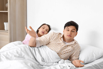Young annoyed man lying in bed with his snoring wife at home