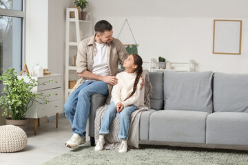 Apologetic father hugging his daughter on sofa at home