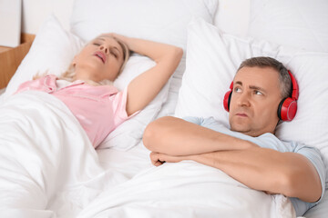 Mature man with headphones cannot sleep because of his wife's snoring in bedroom