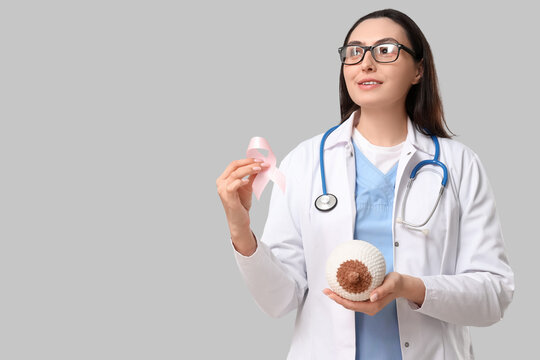 Female doctor with pink awareness ribbon and knitted breast model on light background