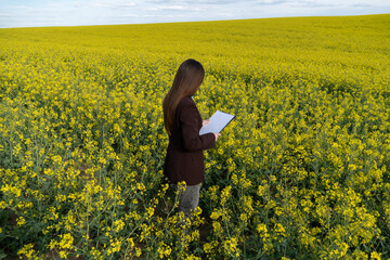 Fototapeta premium Woman with clipboard in rapeseed field, checking cultivation progress, analyzing data, agriculture business, rural scene, yellow flowers